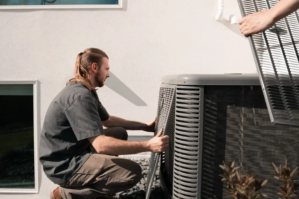 An All Seasons HVAC technician removing the access panel of an outdoor air-conditioning condenser unit at a home
